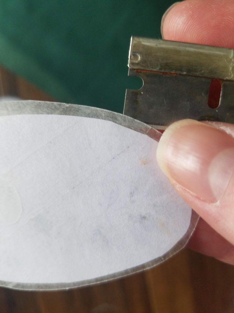 Using a razor blade to separate wax paper from back of sticker